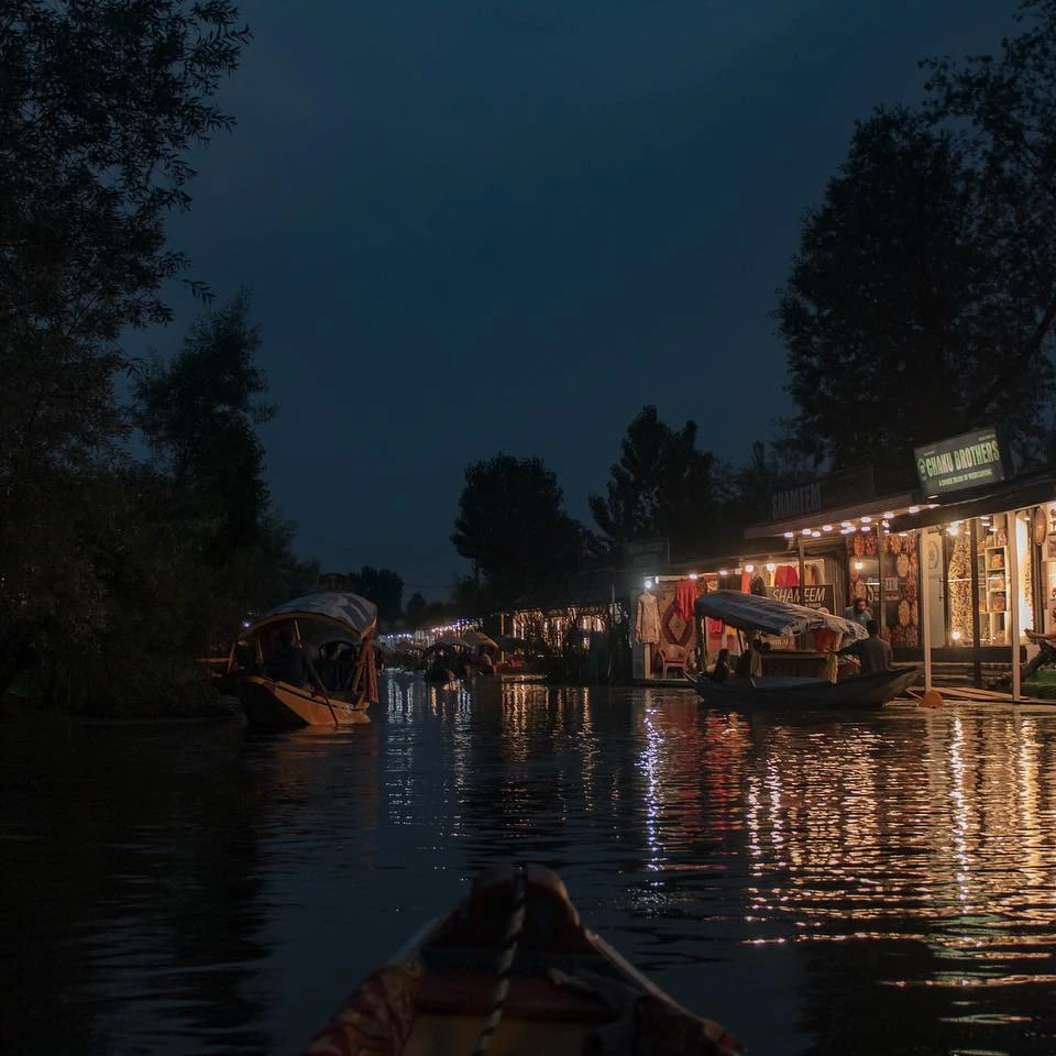 Boats beside illuminated waterfront buildings, with reflections on dark water.