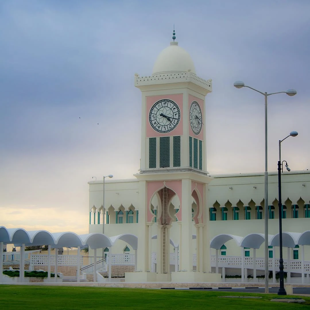 A pale clock tower with a dome beside an arched colonnade.