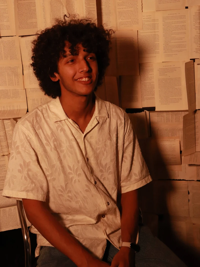 Nawaar seated against a wall covered with book pages.